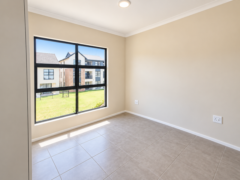 A bright, empty bedroom featuring neutral tiled flooring, a large black-framed window, and clean, well-maintained walls.