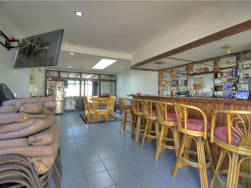 A spacious entertainment area featuring a built-in wooden bar with mirrored shelving, tiled flooring, and a skylight, offering potential for modern updates.