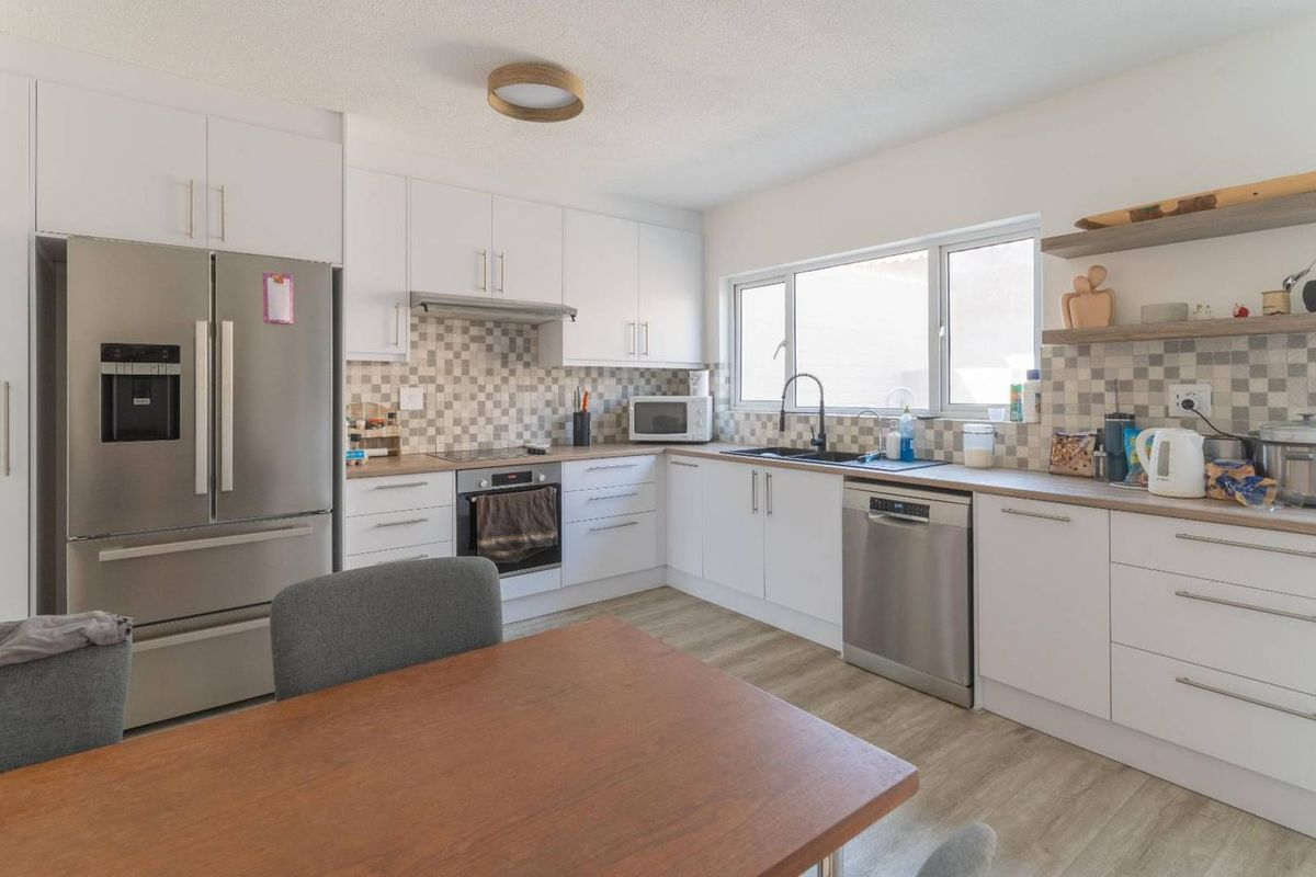 A bright, modern kitchen featuring white cabinetry, wood-look countertops, a tiled backsplash, and integrated stainless steel appliances.