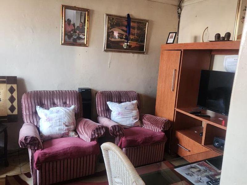 A living room area featuring tiled flooring and decorative ceiling molding, currently showing signs of wear and requiring cosmetic updates.