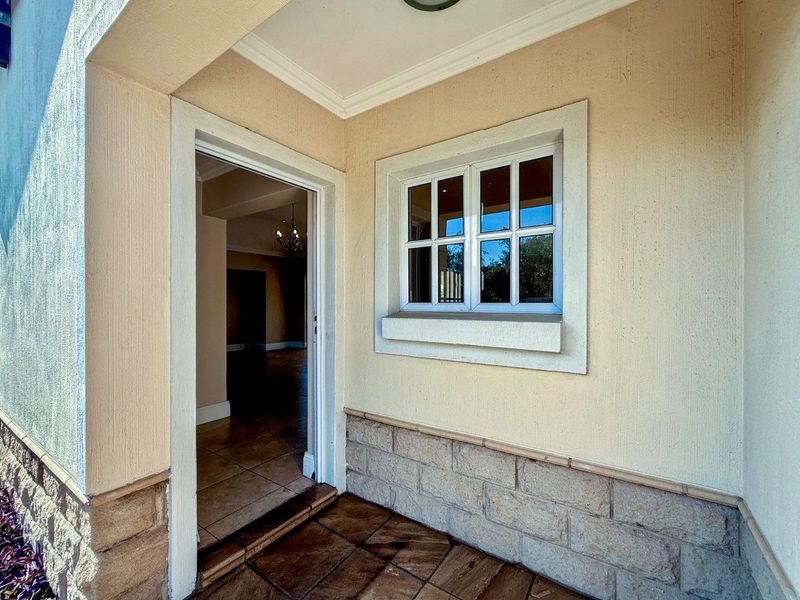 A covered entrance area featuring stone cladding, tiled flooring, and a classic window frame leading into the home's interior.
