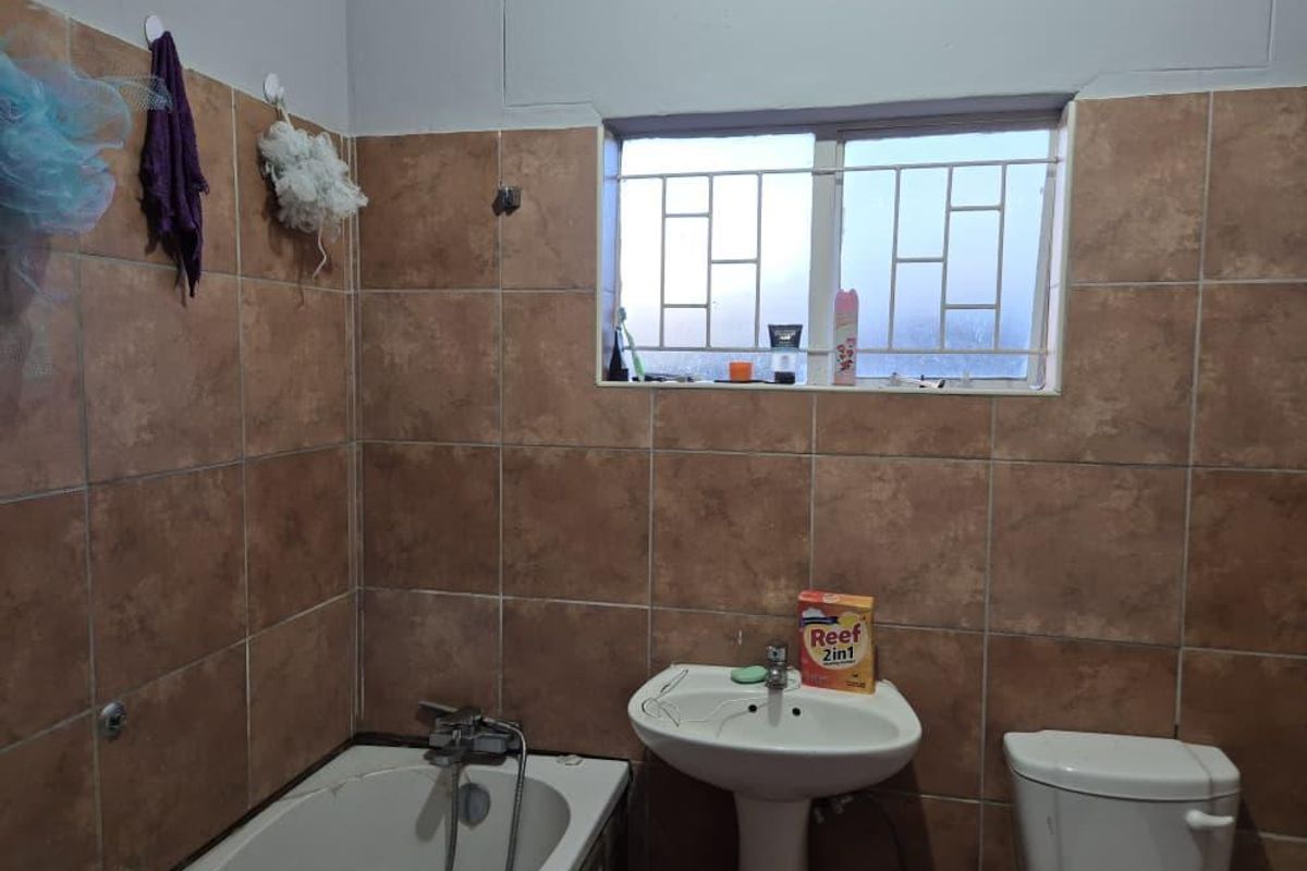 A functional bathroom featuring a pedestal basin, bathtub, and toilet, finished with brown wall tiling and security bars on the window.