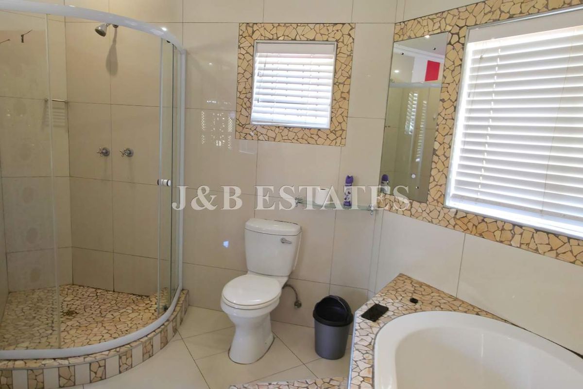 A functional bathroom featuring a corner shower enclosure, a standard toilet, and a built-in bathtub with decorative mosaic tile accents.