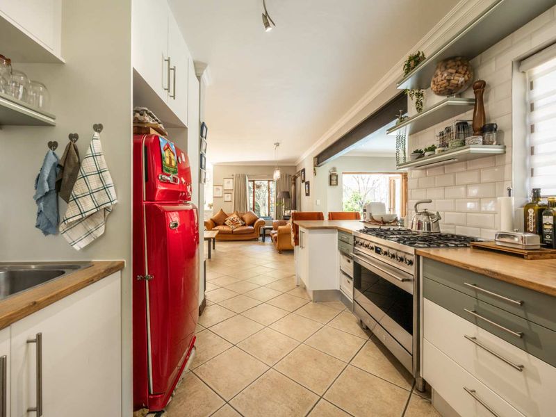 Open-plan kitchen featuring a gas cooktop, subway tile backsplash, and floating shelves, flowing seamlessly into the adjacent living area with tiled flooring throughout.