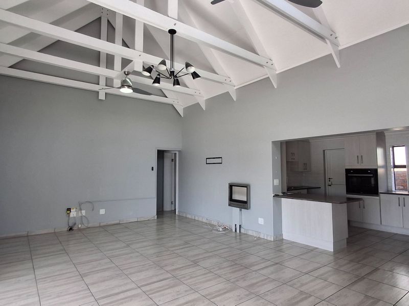 Spacious open-plan living area featuring a high vaulted ceiling with exposed rafters, tiled floors, and a modern kitchen with built-in appliances and breakfast counter.