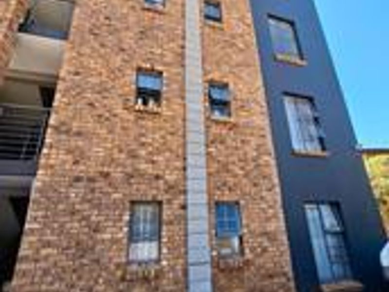 A low-angle view of an apartment building facade featuring a combination of face brick and dark painted plaster finishes with aluminium window frames.