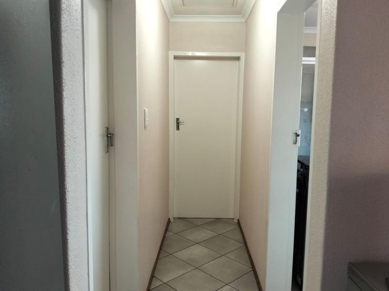 A clean and functional hallway featuring neutral wall finishes, tiled flooring, and multiple internal doors providing access to adjacent rooms.