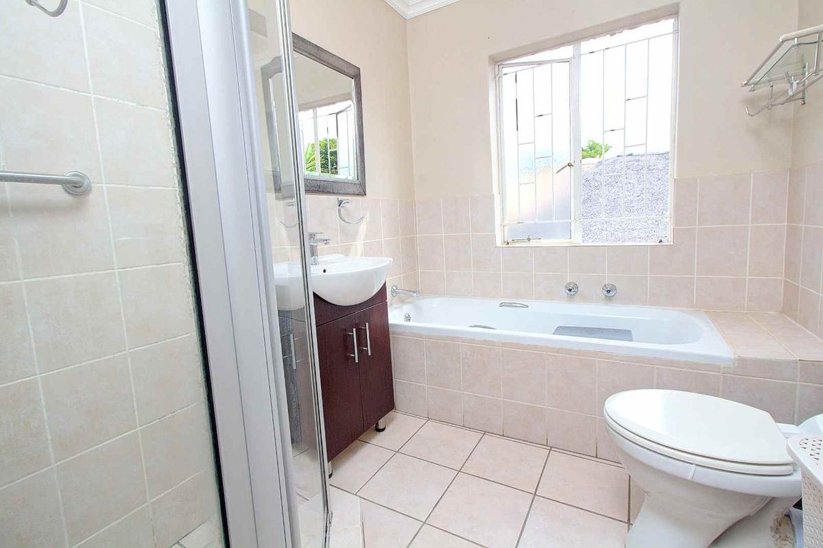 A functional bathroom featuring a built-in bathtub, separate glass-enclosed shower, vanity basin, and tiled flooring with neutral wall finishes.