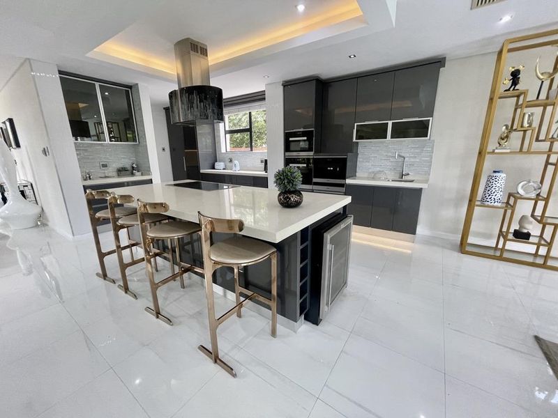 Modern kitchen featuring high-gloss cabinetry, a large central island with quartz countertops, integrated appliances, and sophisticated recessed lighting.