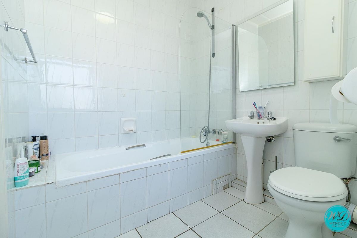 A functional bathroom featuring a bathtub with a glass shower screen, pedestal basin, and toilet, finished with white wall and floor tiles.