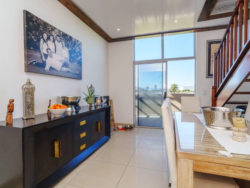 Bright dining area featuring tiled flooring, a wooden staircase, and a large sliding glass door providing access to an outdoor balcony.