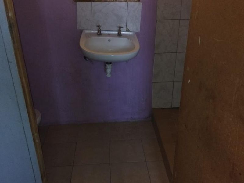 A compact bathroom featuring a wall-mounted basin, tiled flooring, and security bars on the window, requiring cosmetic updates to modernize the space.