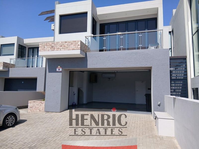 Modern apartment exterior featuring a paved driveway, double garage, and an upper-level balcony with glass balustrades and folding doors.