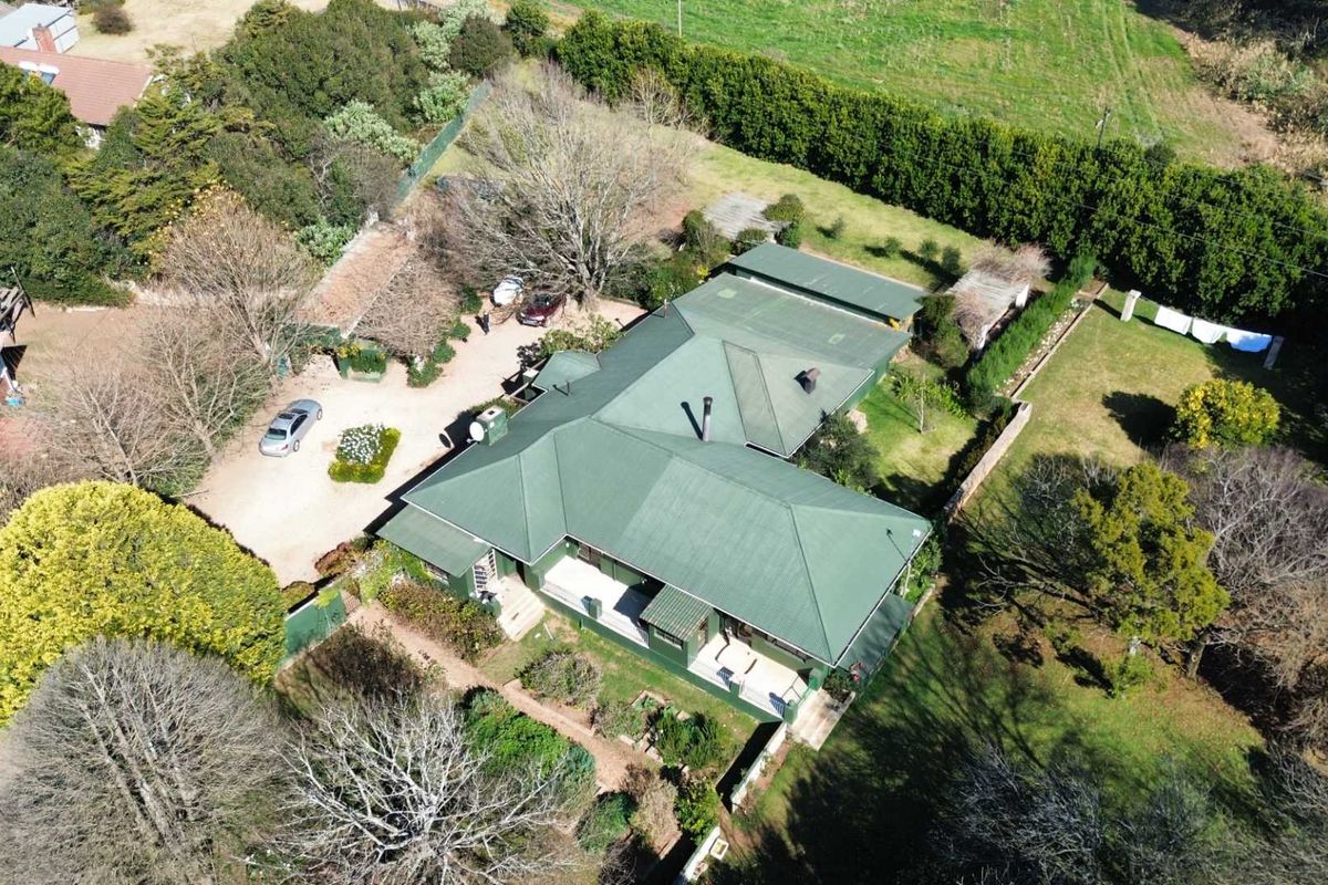 Aerial view of a residential property featuring a green metal roof, surrounding garden areas, and a driveway with parking space.