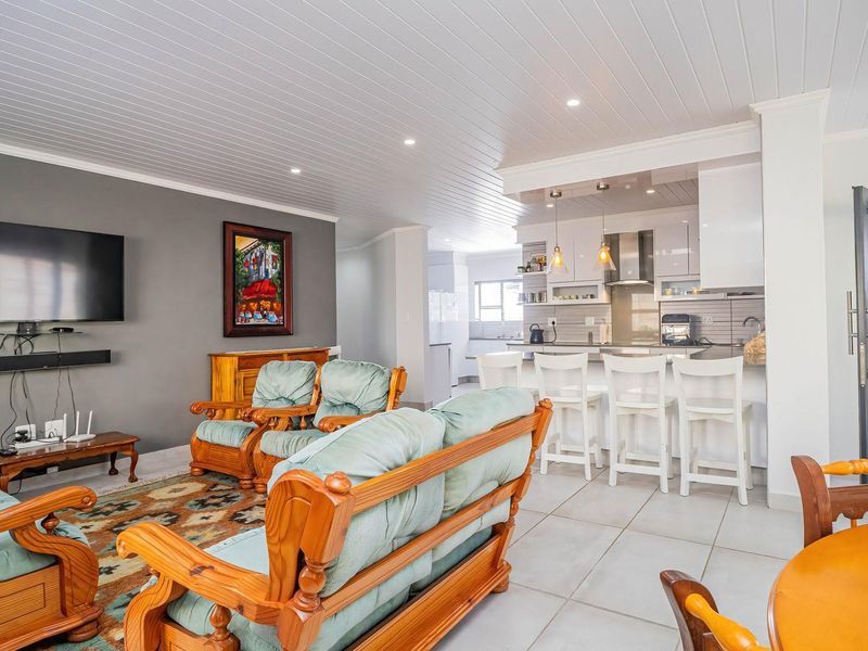 Spacious open-plan living area featuring a modern kitchen with breakfast bar, tiled floors, and a distinctive tongue and groove ceiling.