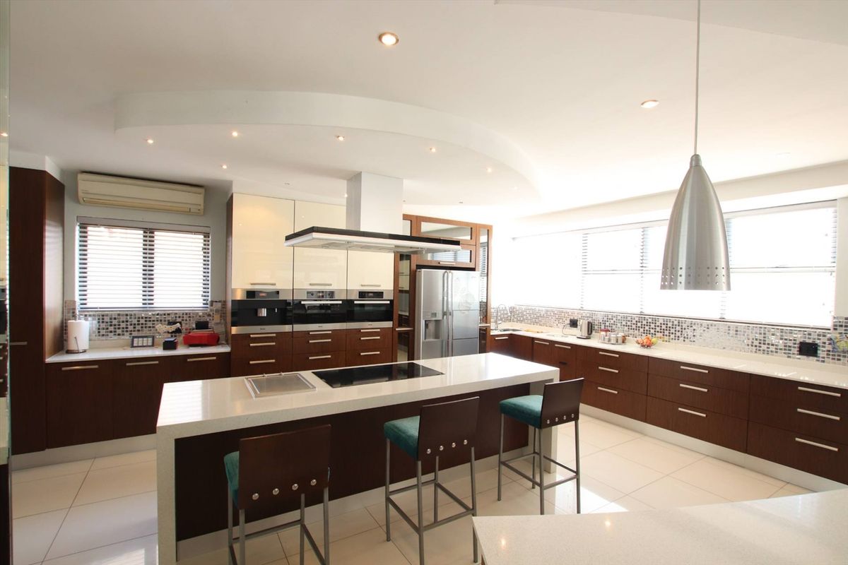 Modern kitchen featuring a large central island with integrated cooktop, sleek cabinetry, mosaic tile backsplash, and recessed ceiling lighting.