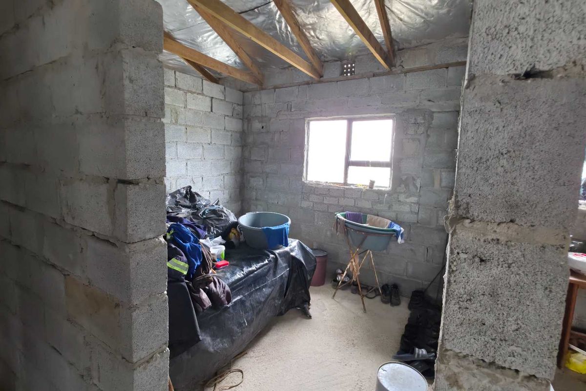An unfinished bedroom space featuring exposed concrete block walls, timber roof trusses, and reflective insulation, offering a blank canvas for renovation and interior finishing.
