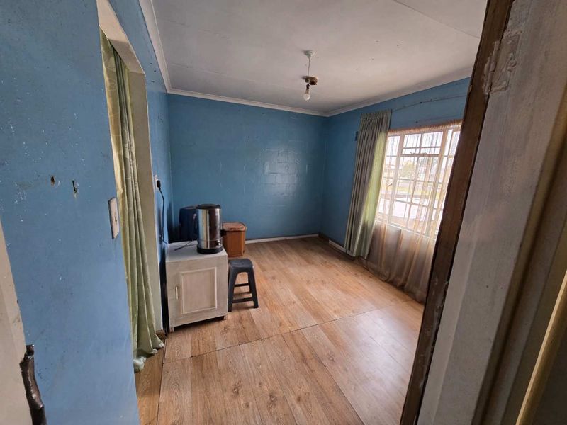 A vacant bedroom featuring laminate flooring and a steel window frame, requiring cosmetic updates and wall repairs to restore its appeal.