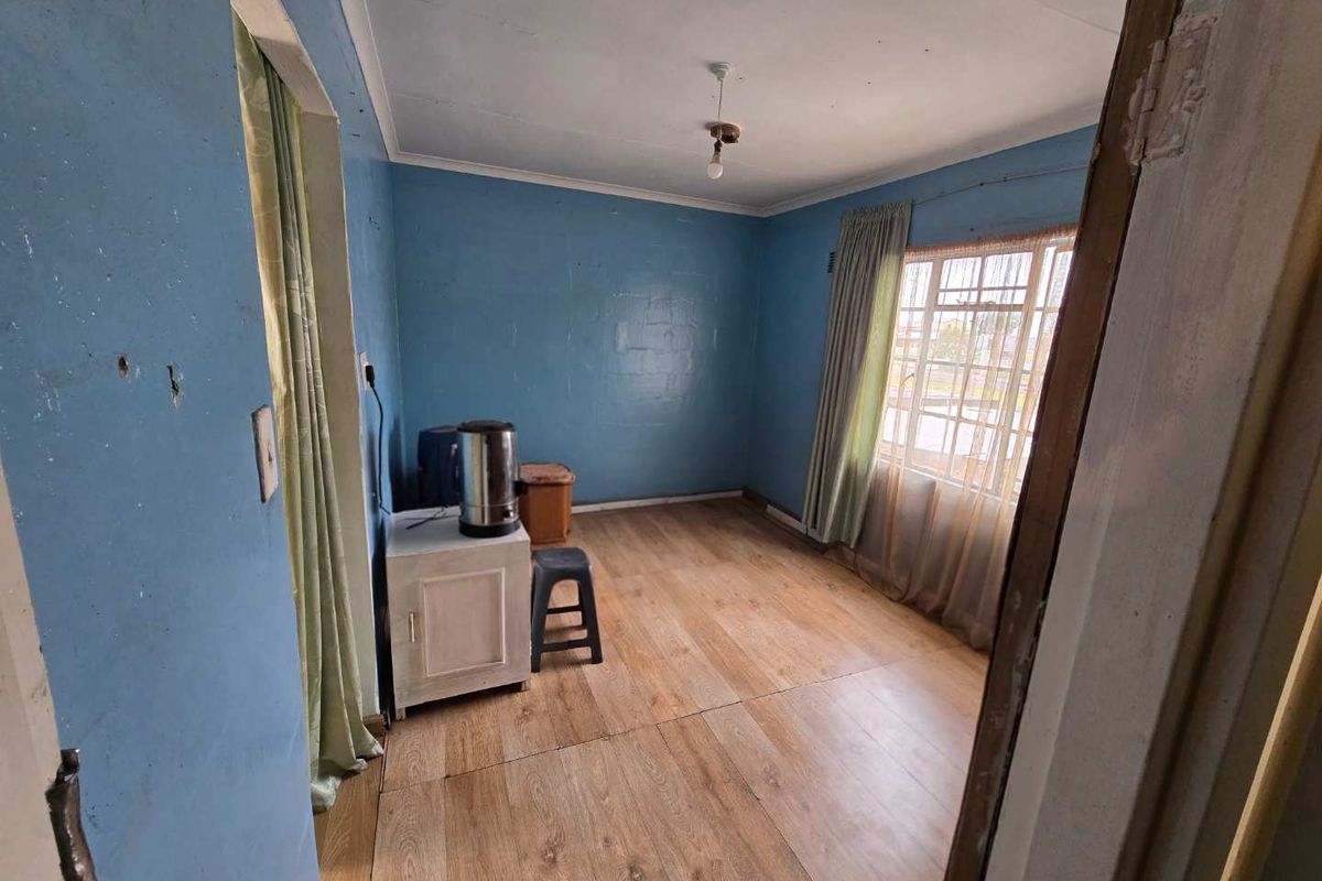 A vacant bedroom featuring laminate flooring and a steel window frame, requiring cosmetic updates and wall repairs to restore its appeal.