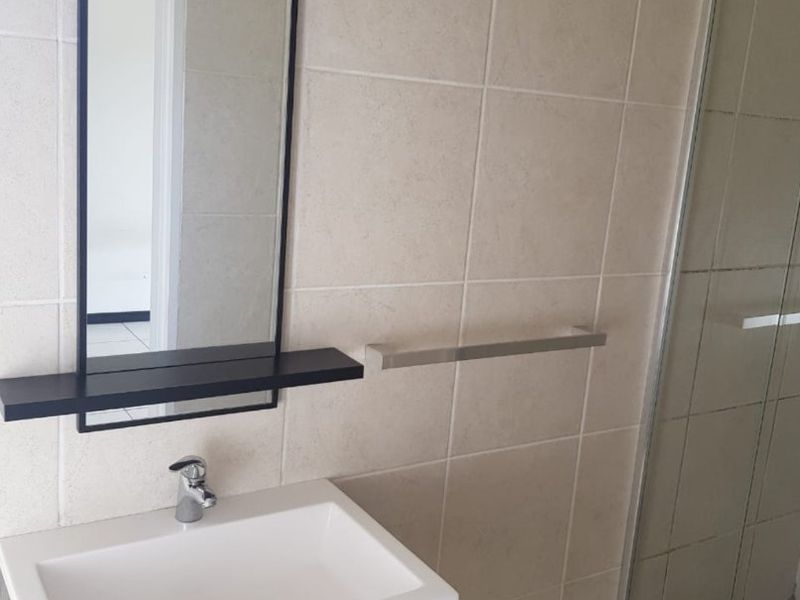 A modern bathroom featuring a wall-mounted vanity with integrated basin, a framed mirror, and a glass-enclosed shower with neutral ceramic tiling.