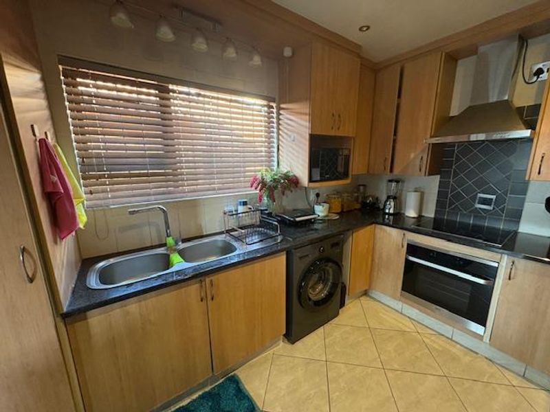 Functional kitchen featuring light wood cabinetry, dark countertops, built-in oven, electric hob, stainless steel extractor, and tiled flooring.