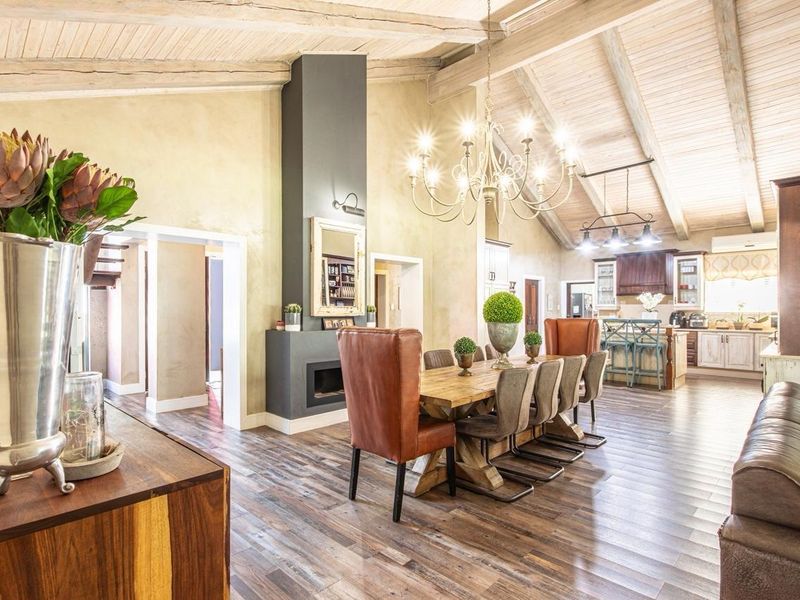 Spacious open-plan living and dining area featuring high vaulted ceilings with exposed timber beams, a central fireplace, and a well-appointed kitchen.