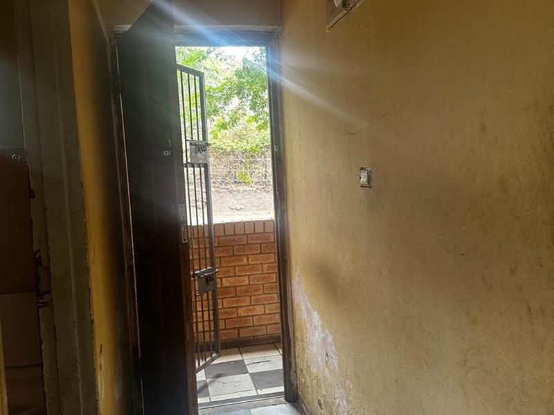 An entry area featuring tiled flooring and a security gate, showing significant wear to wall finishes and requiring cosmetic refurbishment.