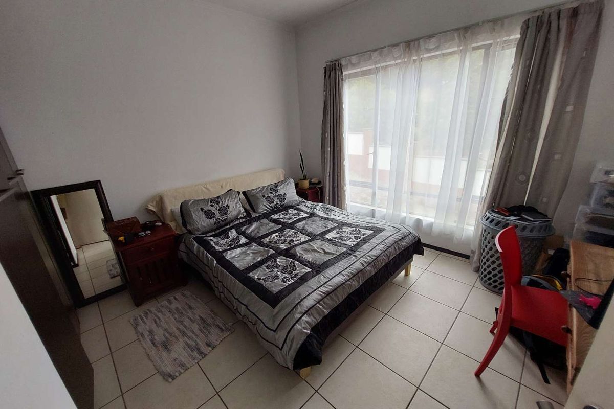 A bedroom featuring tiled flooring and large windows with curtain tracks, providing natural light and access to the exterior.