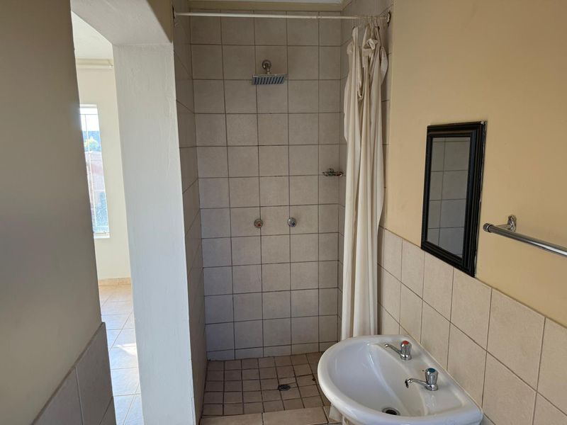 A functional bathroom featuring a tiled shower enclosure and a pedestal basin, requiring cosmetic updates to improve its overall condition and aesthetic appeal.