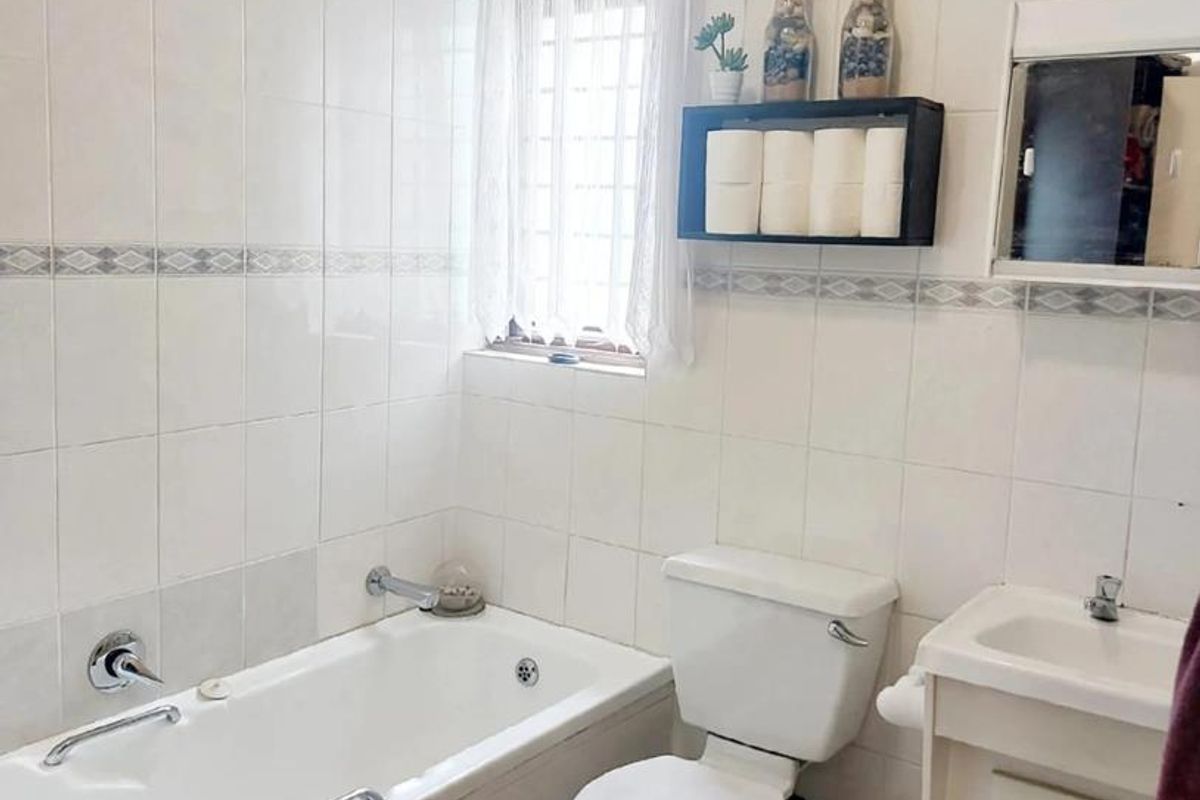 A functional bathroom featuring a bathtub, toilet, and vanity basin with full-height wall tiling and tiled flooring.