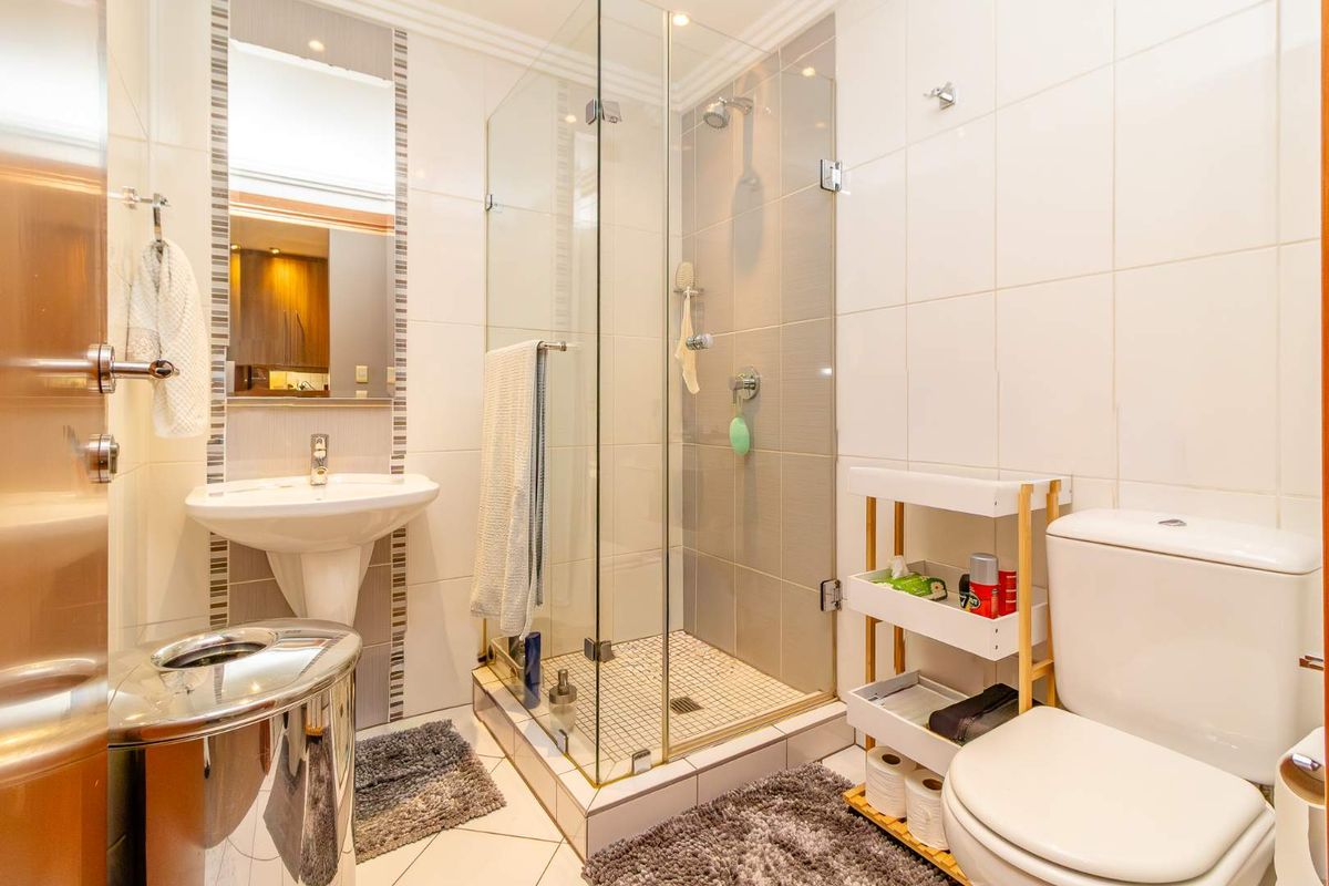 A compact, well-maintained bathroom featuring a glass-enclosed shower, pedestal basin, and toilet with neutral wall tiling.