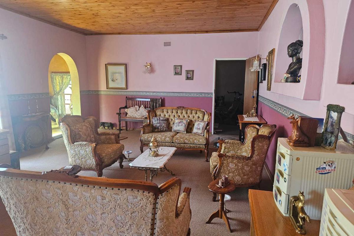 A spacious living room featuring a timber-clad ceiling, arched doorways, and a traditional layout with carpeted flooring.
