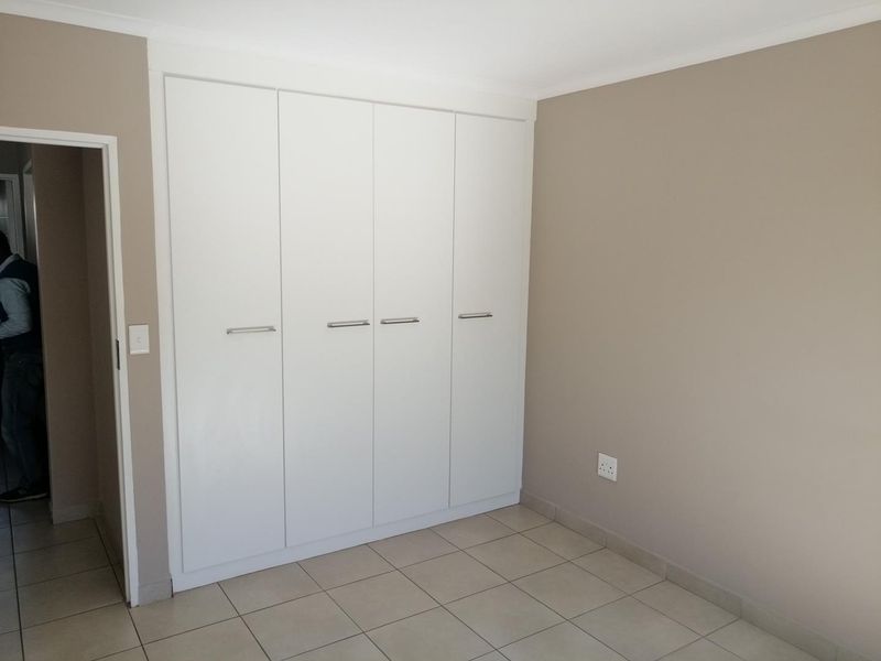 A clean, empty bedroom featuring neutral wall tones, tiled flooring, and modern white built-in cupboards with sleek handles.