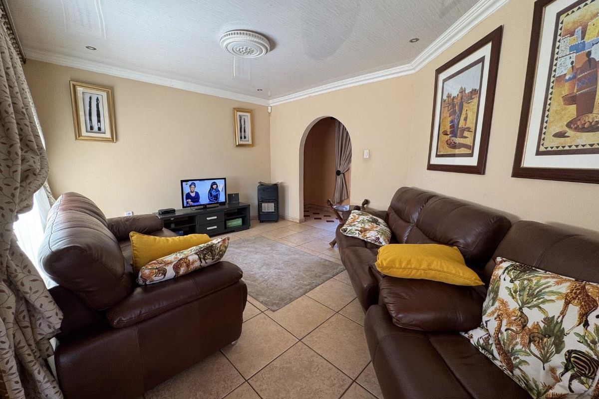 A comfortable living room featuring tiled flooring, decorative ceiling rose, and an arched doorway leading to adjacent spaces.