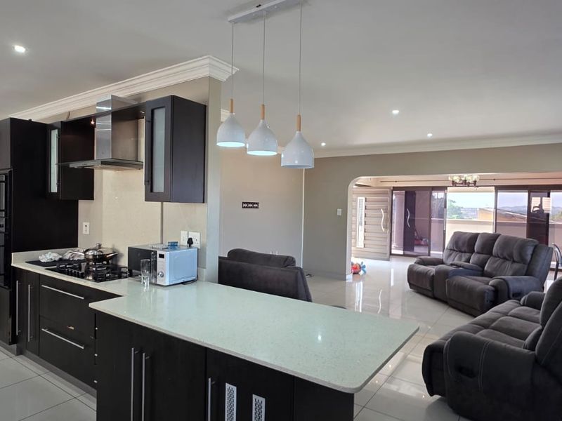 Spacious open-plan kitchen and living area featuring modern dark cabinetry, stone countertops, tiled floors, and seamless flow to an outdoor patio area.