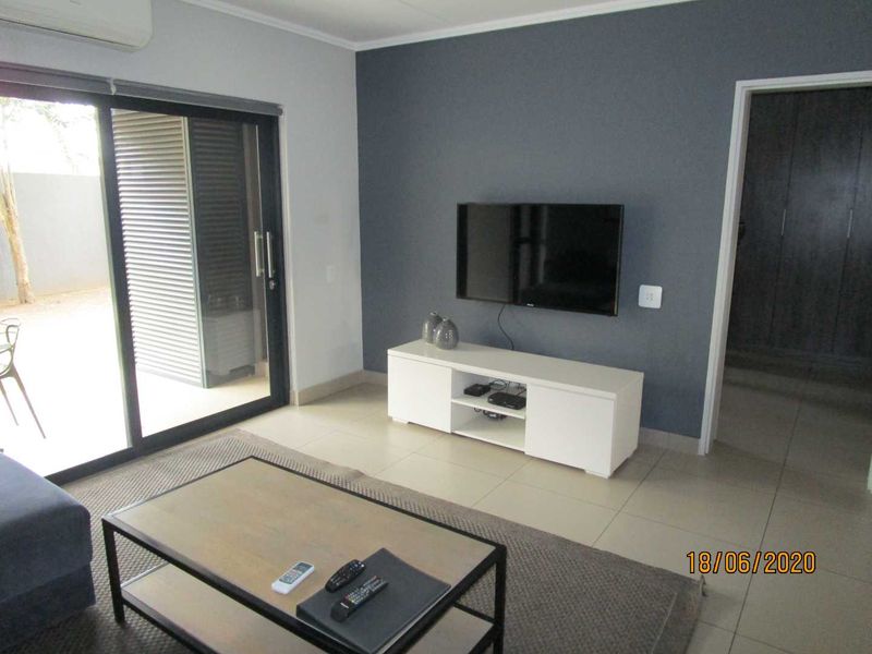 A modern living room featuring tiled floors, a dark grey accent wall, and a large sliding glass door providing access to the outdoor area.