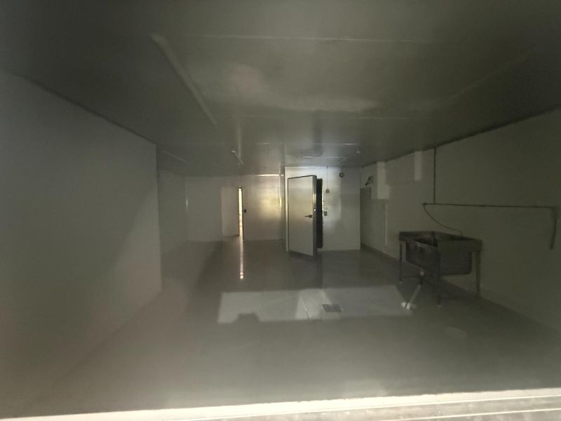 A spacious, empty utility or prep area featuring a stainless steel sink, floor drainage, and a walk-in cold storage unit door.
