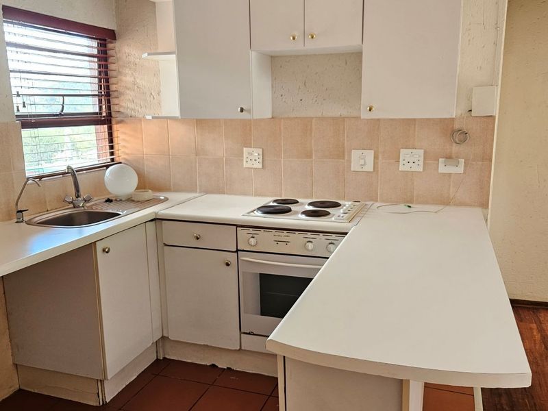 A compact, functional kitchen featuring white built-in cabinetry, laminate countertops, an electric oven and hob, and tiled backsplash, ready for a modern update.