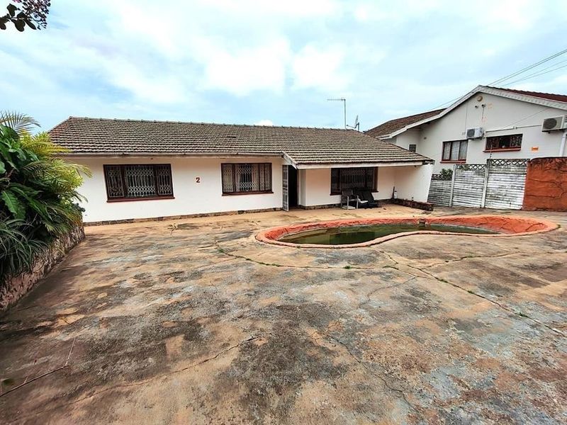 Rear exterior view of the house featuring a concrete patio area and an in-ground swimming pool with visible wear to the paving and finishes.