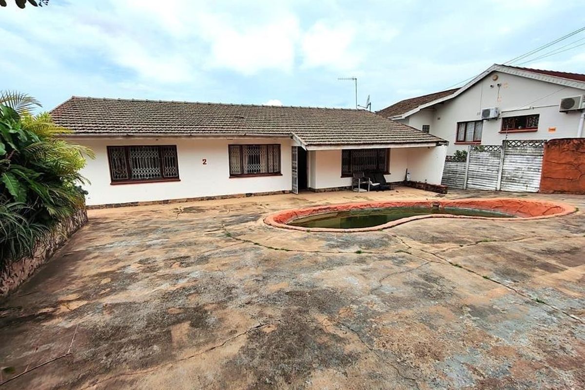 Rear exterior view of the house featuring a concrete patio area and an in-ground swimming pool with visible wear to the paving and finishes.
