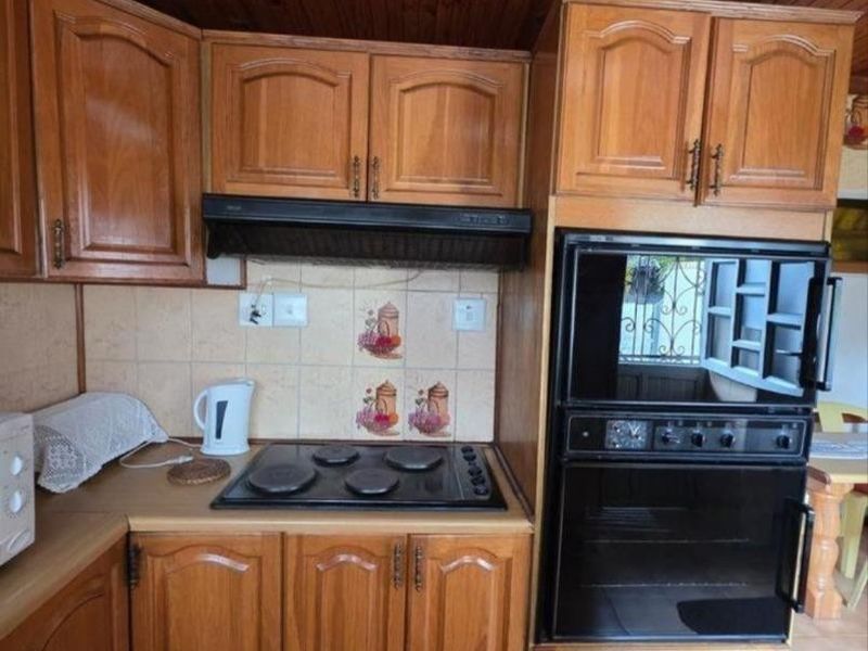 A functional kitchen featuring traditional wooden cabinetry, a built-in oven, electric hob, extractor fan, and a distinctive timber-paneled ceiling.