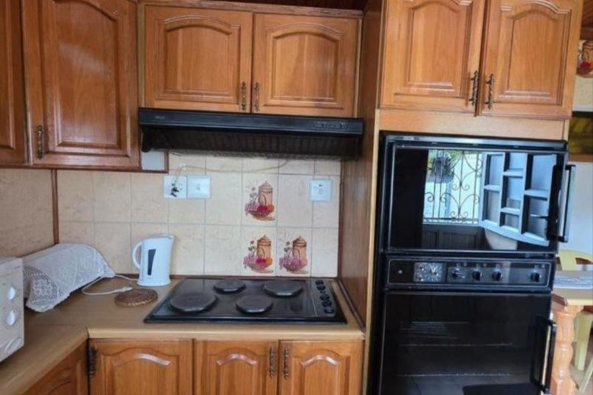 A functional kitchen featuring traditional wooden cabinetry, a built-in oven, electric hob, extractor fan, and a distinctive timber-paneled ceiling.