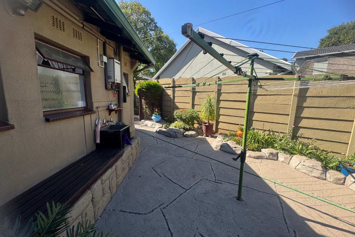 A functional rear exterior area featuring a paved courtyard, a fixed utility sink, a wall-mounted gas geyser, and a rotary clothesline.