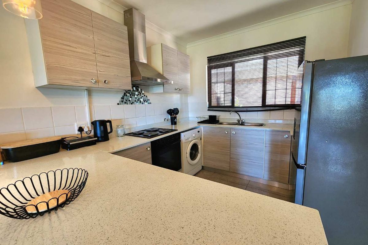 A functional kitchen featuring light wood-grain cabinetry, stone-look countertops, a stainless steel extractor fan, and integrated laundry plumbing.