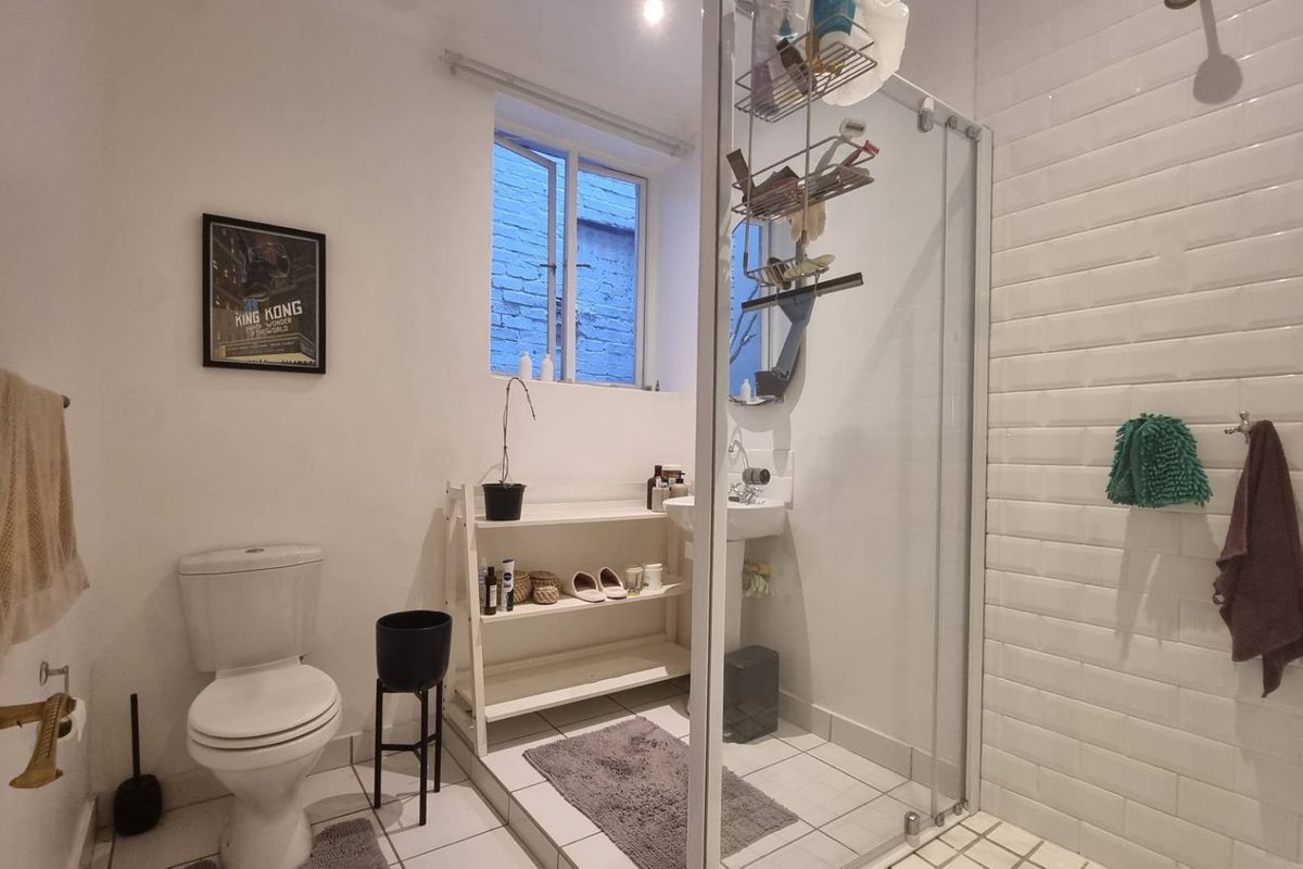 A functional bathroom featuring a glass-enclosed shower with white subway tiling, a pedestal basin, and a standard toilet.