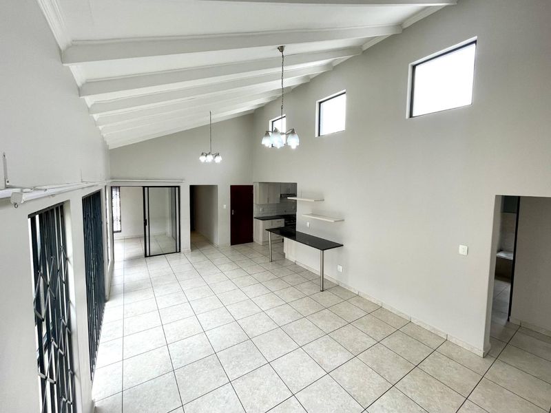 Spacious open-plan living area featuring vaulted ceilings with exposed beams, tiled flooring, and a built-in breakfast bar, offering a bright and versatile layout.