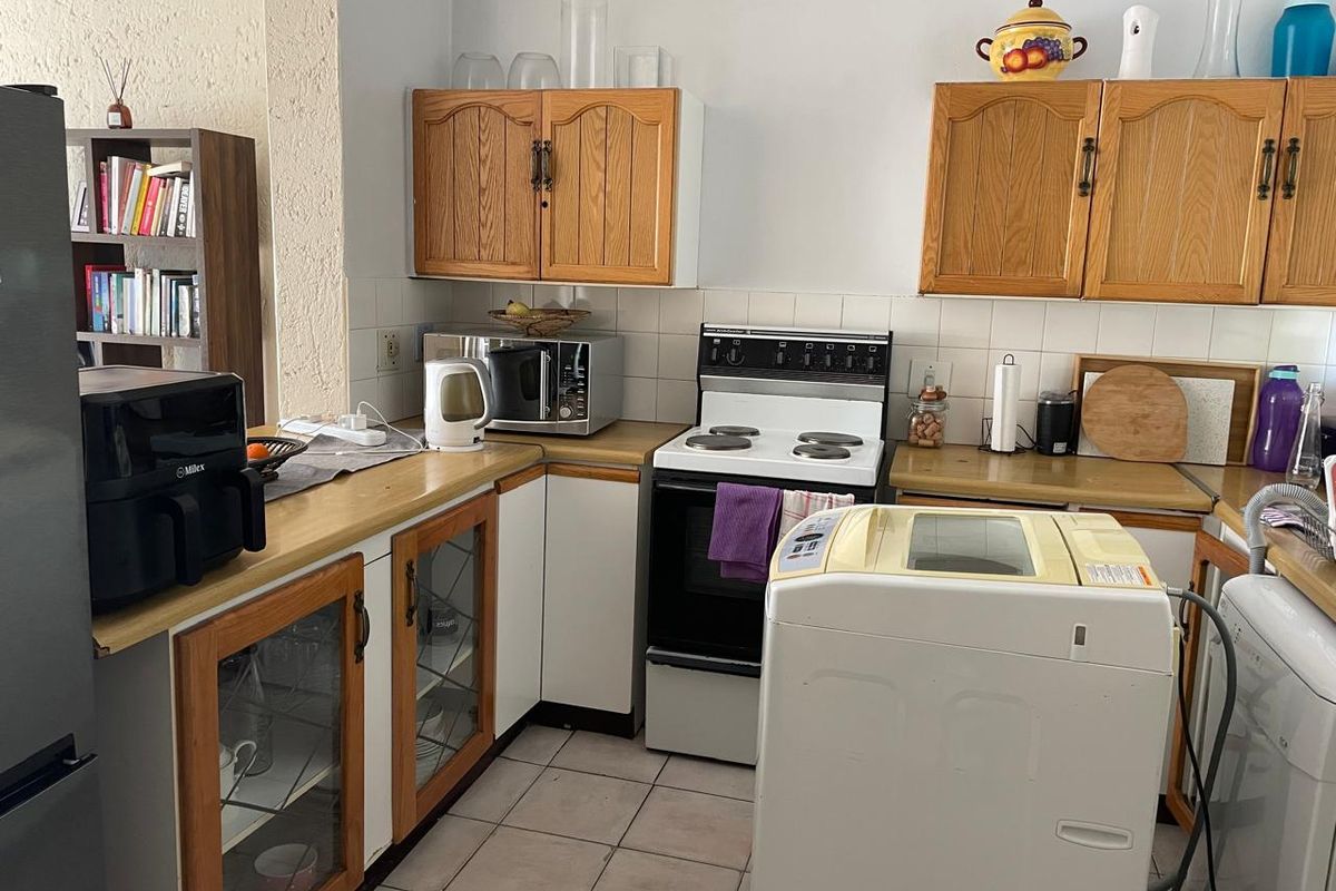 A functional kitchen featuring dated timber cabinetry, laminate countertops, a tiled backsplash, and a freestanding stove, offering potential for modern renovation.