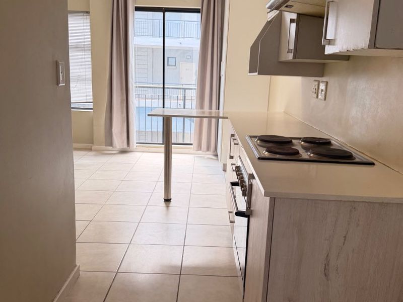 Open plan kitchen and living area featuring tiled floors, built-in cabinetry, electric hob, oven, and access to a balcony through sliding glass doors.