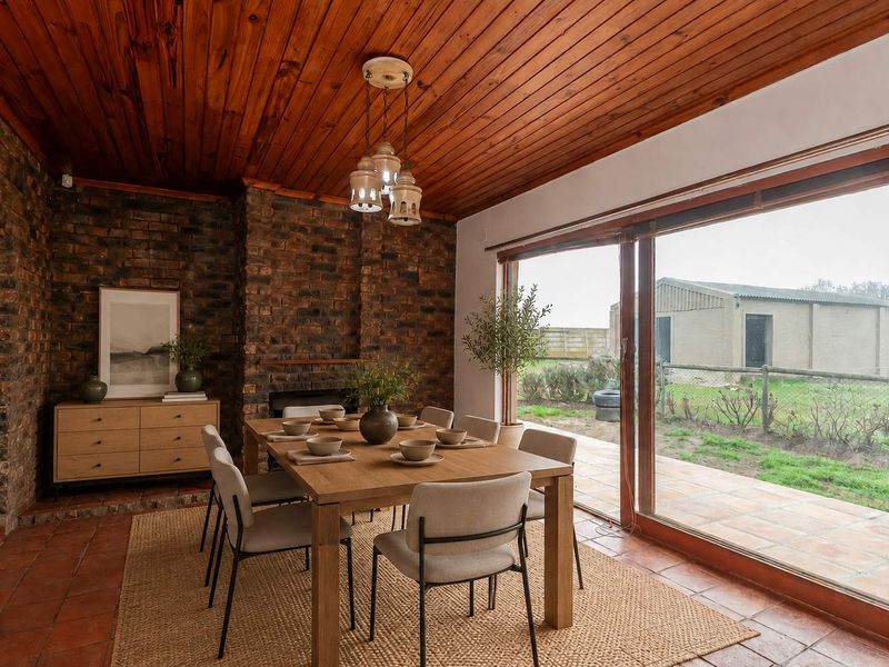 Dining room featuring exposed brick walls, warm timber ceiling, terracotta flooring, and large sliding glass doors providing access to the outdoor patio area.
