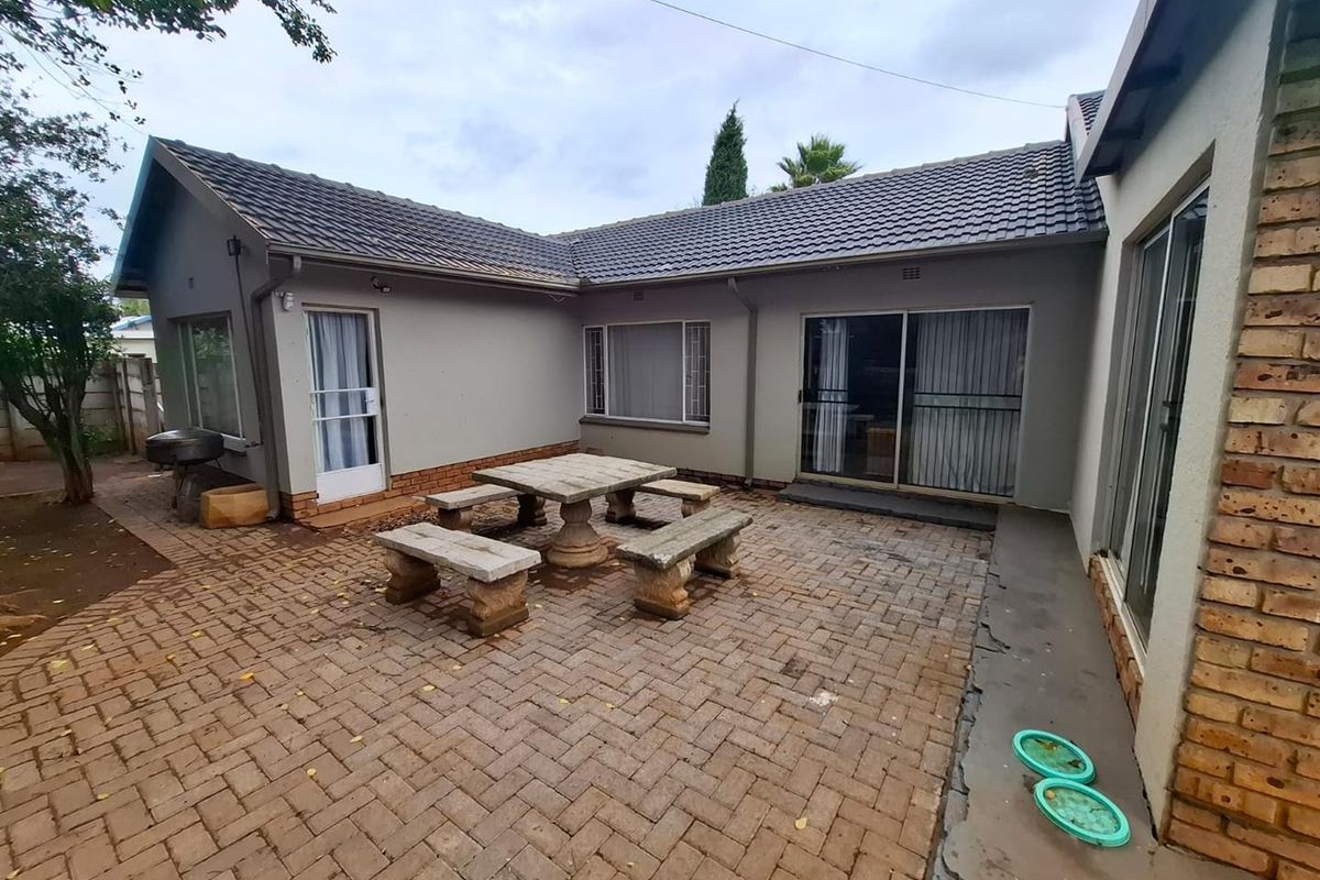 A rear exterior view featuring a paved patio area, sliding glass doors, and a tiled roof, providing a functional outdoor space for entertaining.